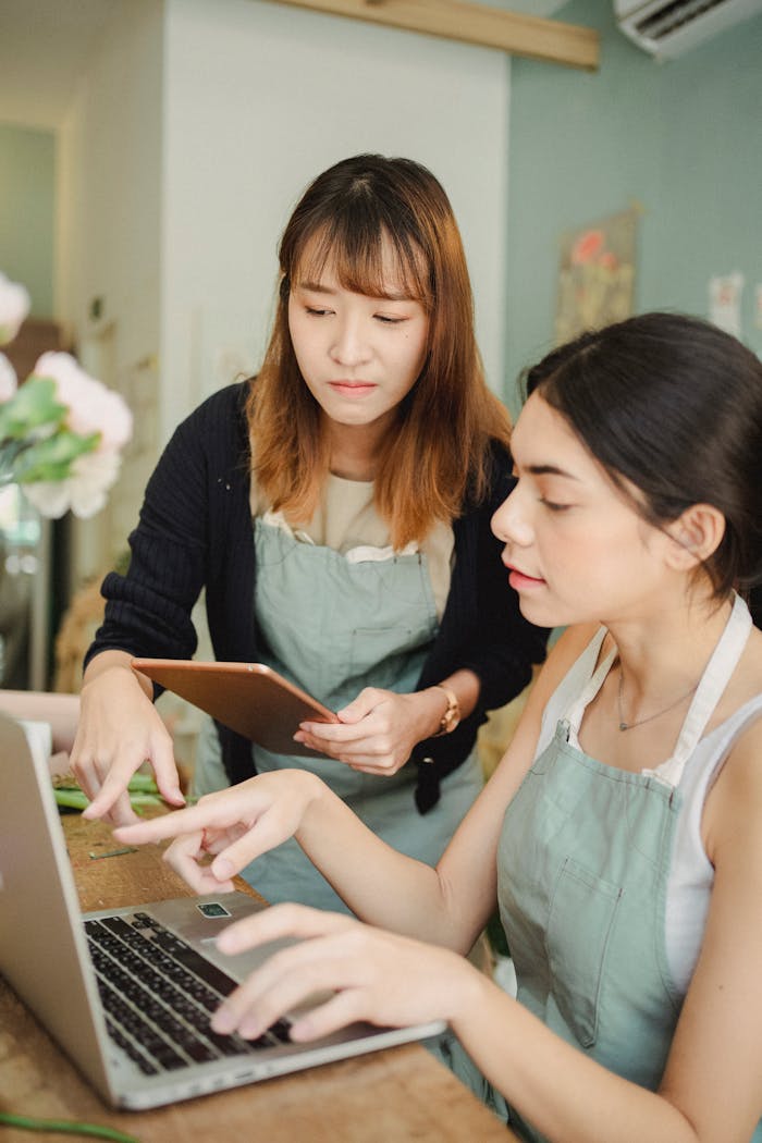 Focused multiethnic female colleagues in floral store at table working on computer while checking orders in internet during work in floristry studio